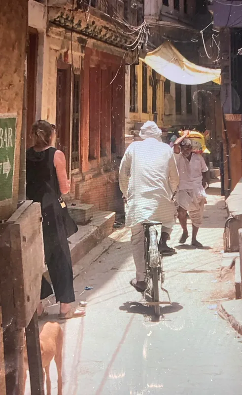 Een foto van een smal straatje met een man in het wit op een fiets.