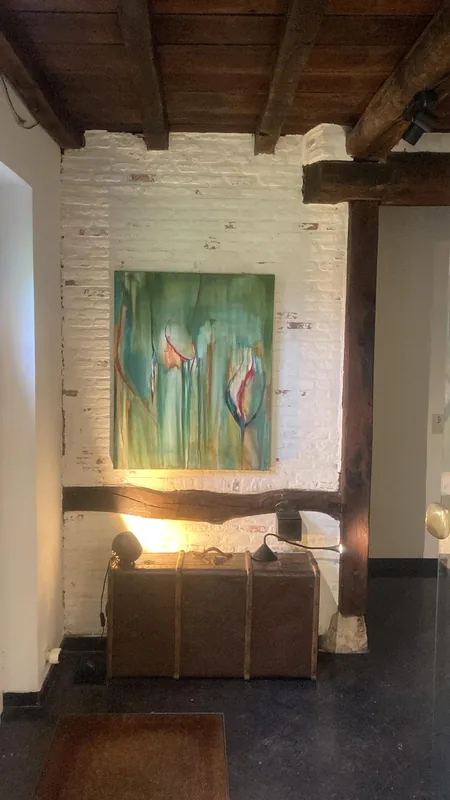 Een groen schilderij met tulpen tegen een witte bakstenen muur, onder de balken.